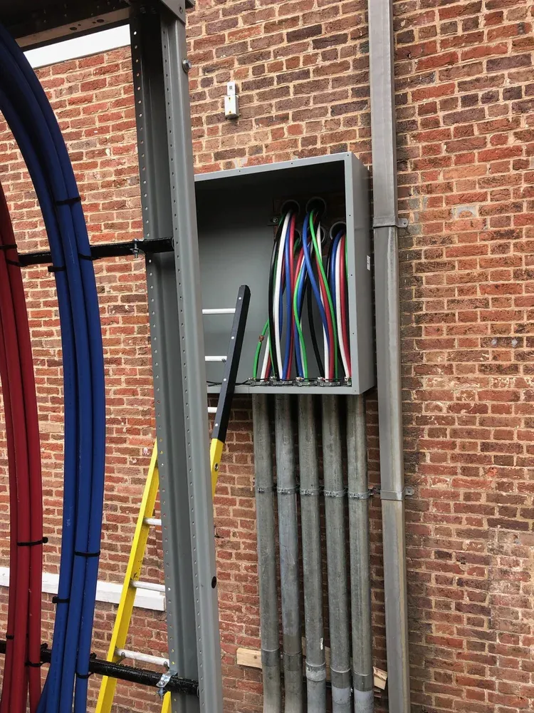Color-coded conductors entering a service gutter on a brick exterior
