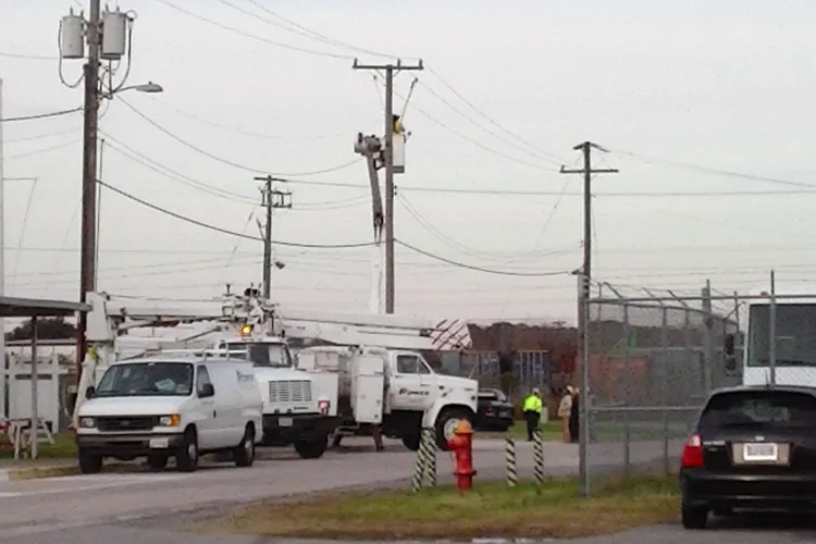 Bucket trucks working on utility poles beside a fenced facility