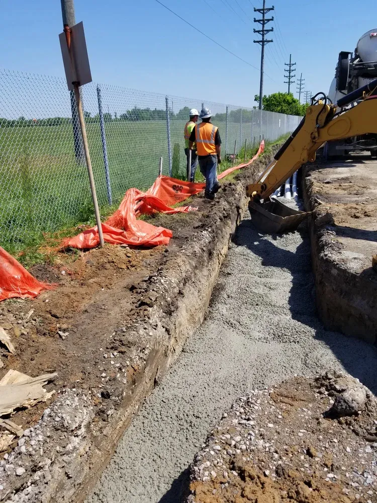 Excavator trenching for underground conduit beside a fence line